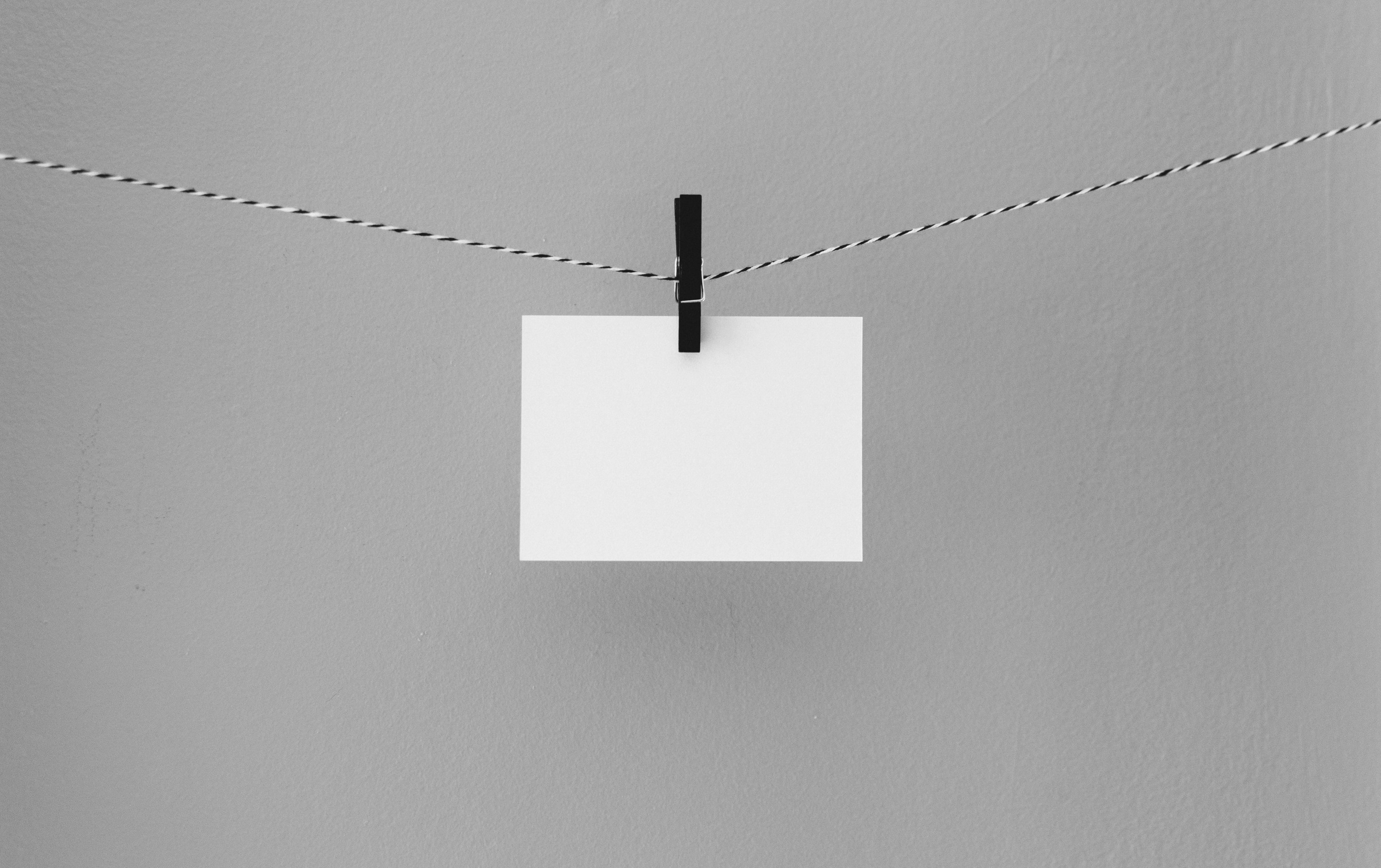 A blank note card suspended from a small paperclip attached to a black and white colored string. Photo by Kelly Sikkema on Unsplash.